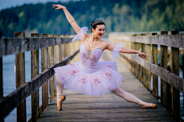 Ballerina performs gracefully in pink tutu on a wooden pier by a serene lake. WA, USA