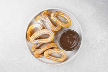 Traditional spanish dessert churros, fried dough pastry dusted with powdered sugar and chocolate sause on white background. Street food, sweet snack, homemade dessert. Top view, copy space