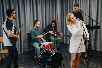 A music band practicing in a studio with a female singer, guitarist, and drummer. The group is...