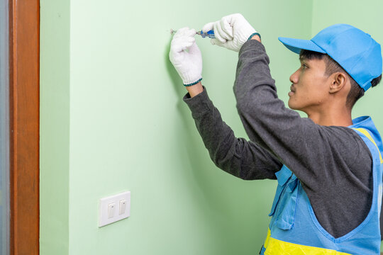 Asian male worker uses screwdriver to tighten screws on gypsum board wall.