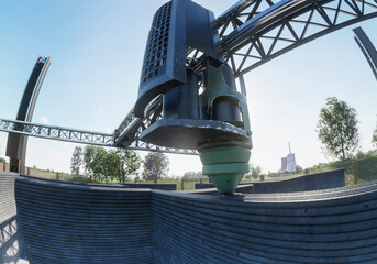 A crane-based 3D printer constructs a concrete building under a clear sky in an open field.