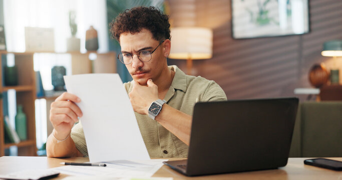 Business, documents and laptop with man in home office for startup planning or research. Computer, reading and remote work with freelance employee at desk in apartment for review of information - Powered by Adobe