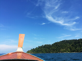 Longtail boat journey on blue sea with green island and bright sky, evoking peaceful and...