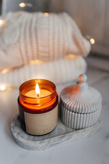 On a plaster tray there is a lighted aromatic soy candle in a brown jar and a plaster casket. Autumn decor and cozy atmosphere. Mockup for candle shop. ?raft label is a place for a logo.