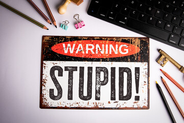 Stupid. Warning Sign on Desk with Keyboard, Pencils, and Stationery Items for Satirical Concept