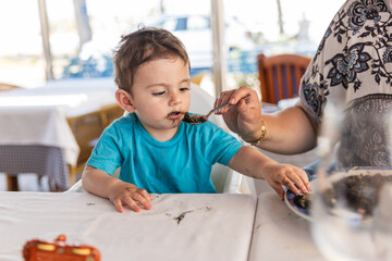 Grandmother feeding one year old grandson with black rice in restaurant
