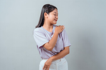 Obraz premium Calm young Asian woman gently touching her shoulder with eyes closed, expressing self-love and serenity. Casual outfit, neutral background, peaceful vibe.