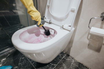 A close-up view of a person wearing yellow gloves cleaning a toilet in a modern bathroom. Cleaning...
