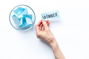 Hand is holding raffle ticket winner near glass jar, top view. Luck and lottery concept