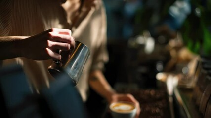 Professional barista carefully pouring steamed milk into ceramic cup, creating intricate latte art with precise hand movements and expert coffee making skills in warm, cozy cafe environment - Powered by Adobe