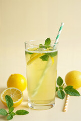 Fototapeta premium Glass of water with lemons, mint leaves and straw on light background