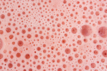 Pink foam texture with small bubbles on a light pink background. Close up macro view of liquid...