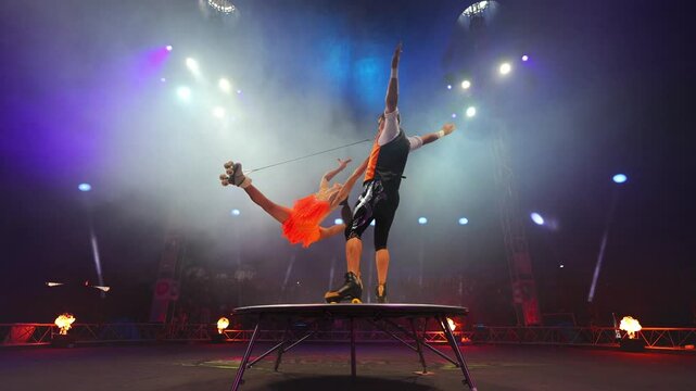 Young pair of acrobats, man and woman, on roller skates perform in a circus on a small round stage.