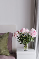 Minimal Bedroom Interior with Fresh Pink Peonies in Glass Vase. Flowers as Home Decor