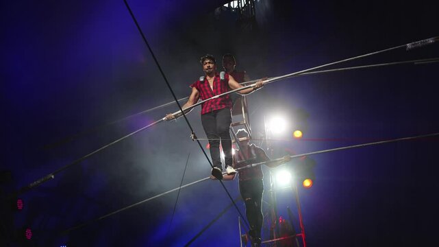 Aerial acrobats hold a rope with a chair on which a tightrope walker stands. A circus trick.
