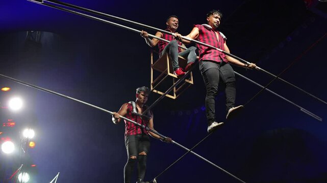 Aerial acrobats hold a rope with a chair on which a tightrope walker stands. A circus trick.