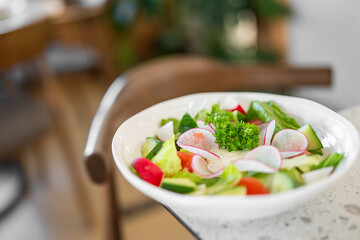 Fresh vegetable salad in a white bowl, featuring sliced radishes, cucumbers, tomatoes, lettuce, and parsley garnish. The vibrant colors and crisp textures highlight its freshness and appeal