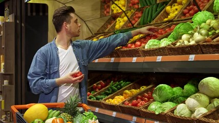 Young man selecting fresh tomatoes and cucumbers at the supermarket