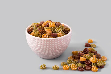 Pasta Rotelli from durum wheat varieties with carrot , spinach and beetroot isolated on a grey background , high-resolution . Side view of the bowl with colored pasta , place for text . 