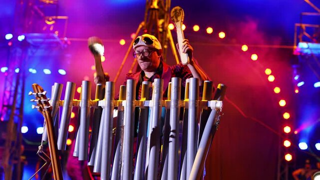 A clown entertains guests in the circus arena in the light of spotlights and smoke, plays a trumpet.
