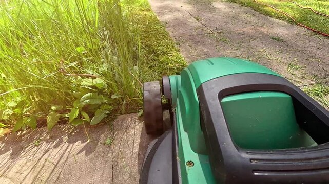 Close up shot of A man mows the grass in the backyard with an electric lawn mower. Slow motion