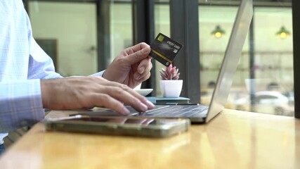 Online transaction with credit card: a man carefully inputs his credit card information on a laptop at a coffee shop. Capturing the convenience of online payment