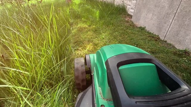 Close up shot of A man mows the grass in the backyard with an electric lawn mower. Slow motion