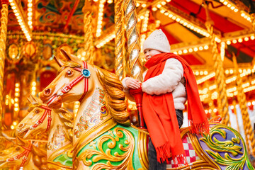 Child enjoying a carousel ride at a festive fairground in winter, surrounded by bright lights and...