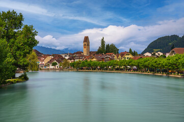 Obraz premium Scenic view of Interlaken, Switzerland, with the Aare River and surrounding Swiss Alps in the background, featuring traditional buildings and lush greenery. Long exposure.