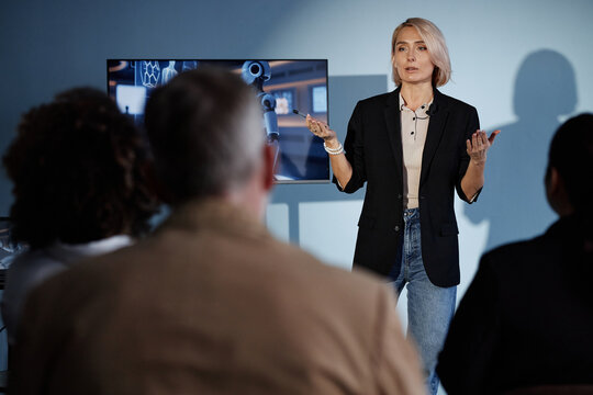 Medium full shot of female speaker delivering presentation on integrating AI into business in packed auditorium, highlighting innovations in emerging technologies