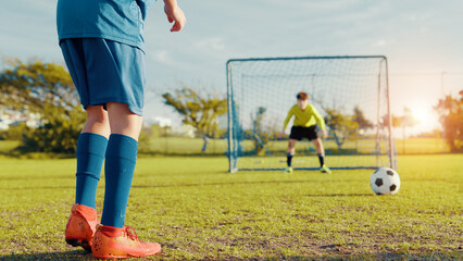 Penalty kick, boys or legs of football player with goalkeeper for outdoor game or match in kids tournament. Sports, children and soccer athlete with ball on grass at practice on field at stadium
