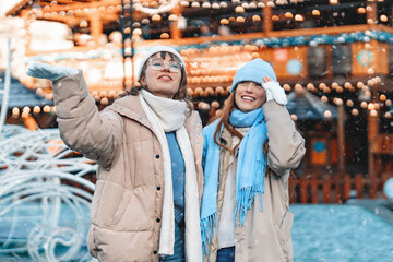 Fototapeta premium Two friends enjoying a snowy day in a festive outdoor market with colorful decorations and warm clothing during winter season