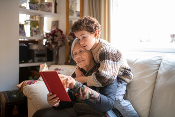 Grandson and grandmother reading a book together on the sofa