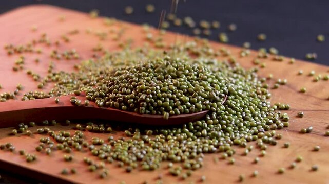 A pile of green mung beans in a wooden spoon  on a wooden board and black background