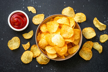 Potato chips and ketchup on black table. Top view.