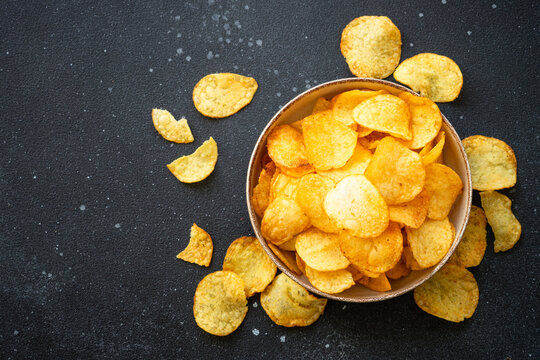 Potato chips and ketchup on black table. Top view.
