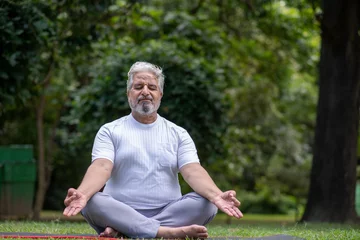 Rolgordijnen Indian Healthy senior man meditating in park, sitting lotus pose on yoga mat outdoor © Pix4Ads