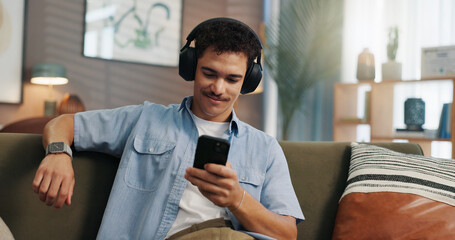 Headphones, man and smile with phone on sofa for social media scroll, streaming service or...