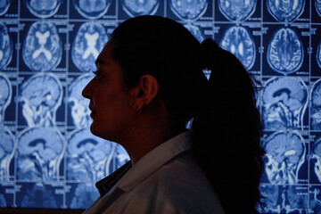 Side view of Middle Eastern female professional neurologist standing against screen displaying brain MRI scan in hospital meeting room