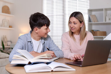 Mother helping her son with homework at table indoors