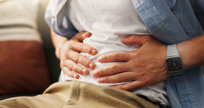 Stomachache, hands and person in home, pain and man with food poisoning in living room or indigestion. Abdominal, cramps and discomfort on couch, gas and bloating in lounge, diarrhea or constipation