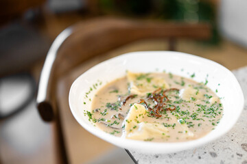 Close-up of a white bowl filled with creamy soup, garnished with caramelized onions and fresh...