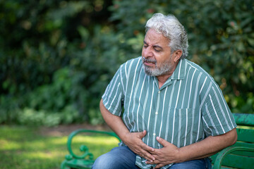Indian painful senior man suddenly suffering 
stomach pain at park