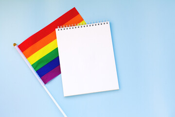 Blank mock up notebook on rainbow LGBTQ flag, blue background. June proud pride month parade, gay marriage, coming out day , human rights, tolerance concept. Flat lay, top view place for text or logo
