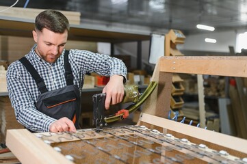 Carpenter using pneumatic stapler to assemble sofa frame in furniture factory