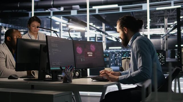 Engineer in data center frustrated by critical error popup on monitor during diagnostics session. IT expert stressed while troubleshooting system fault affecting infrastructure performance, camera A