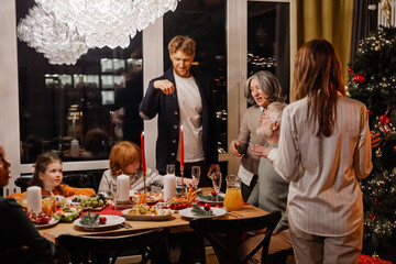A man lights candles with a match while his family and guests stand and sit at the table next to him