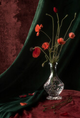 vintage still life with red poppies in a crystal decanter in green and red tones