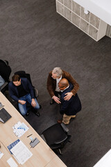 A male employee is standing and has put his hand on the shoulder of a male employee standing next...