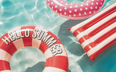 inflatable rings and mattress in white, pink and red colors with polka dots and stripes.   One float prominently displays the words "Hello Summer".  Summer vacation, travel,  tourism concept.